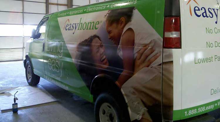 Green and white cargo van wrapped for easyhome, with a lifestyle photo of a parent and child across the side panel, photographed mid-install in a shop bay.