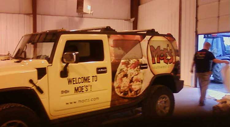 Cream Hummer H2 wrapped for Moe's Southwest Grill, with a food photo and logo on the rear quarter panel and Welcome to Moe's lettering on the door.