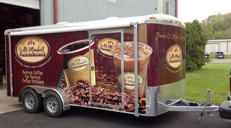 Enclosed trailer wrapped for J.B. Marshall Premium Coffee in deep burgundy, showing oversized hot and iced coffee cups and roasted beans.