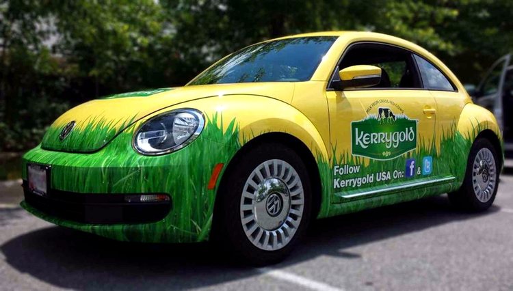 Yellow Volkswagen Beetle wrapped for Kerrygold, with tall green grass graphics running along the lower body and the logo on the door.